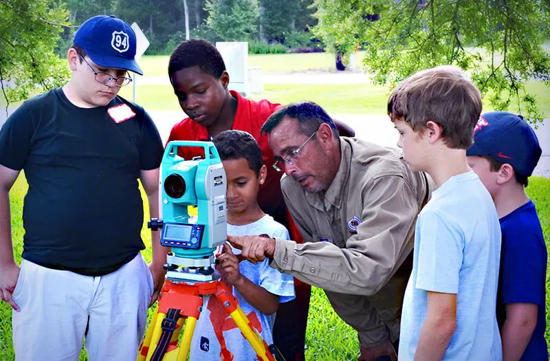 Man showing children how to use a surveying tool